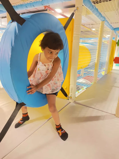 A young girl plays in a colorful indoor playground, holding onto a blue ring.