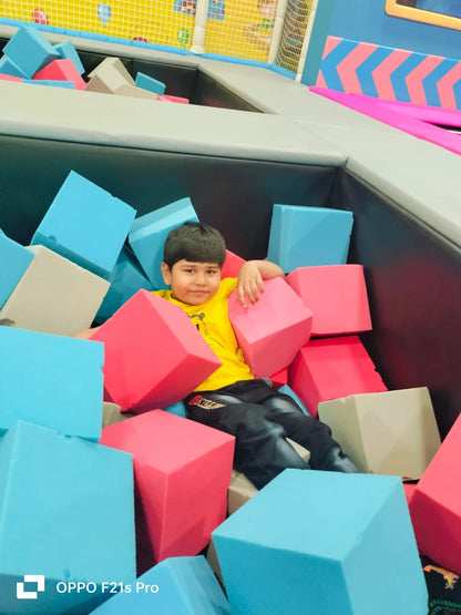 A young boy sits in a ball pit filled with colorful foam cubes.