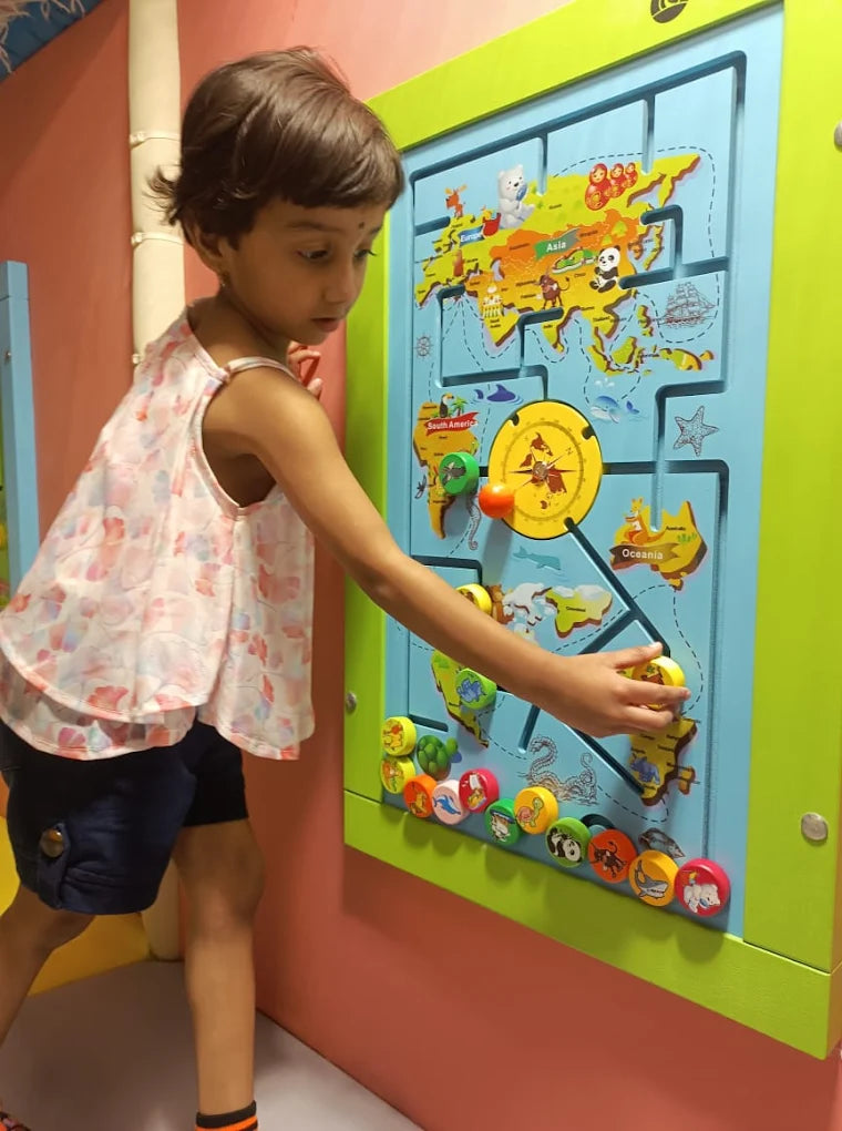 A young child plays with a colorful world map activity board in a playroom.