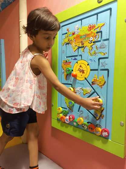 A young child plays with a colorful world map activity board in a playroom.