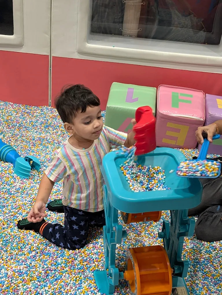 A young child plays with a toy in a ball pit filled with colorful balls.
