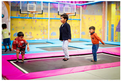 Young children jump on trampolines in an indoor play area with basketball hoops.