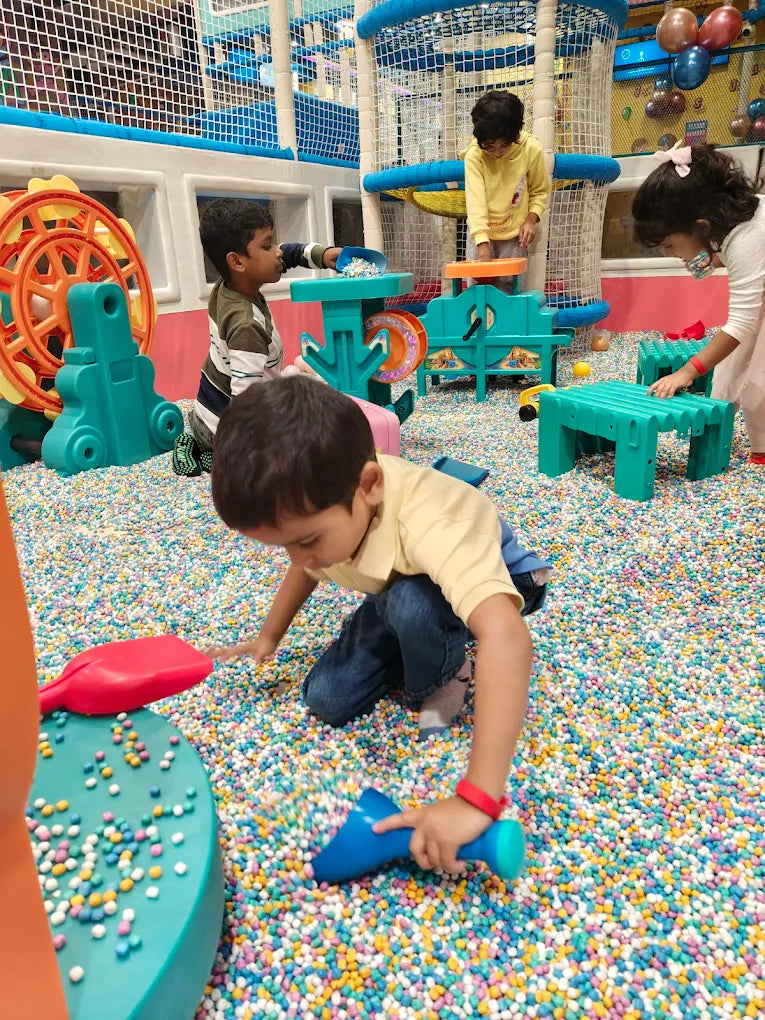 Children play in a ball pit with colorful toys and playground equipment.
