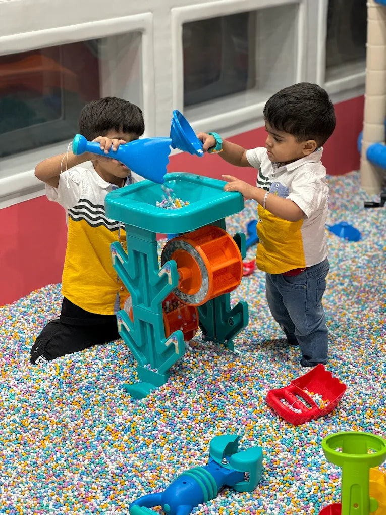 Two young children play with a water toy in a ball pit filled with colorful balls.