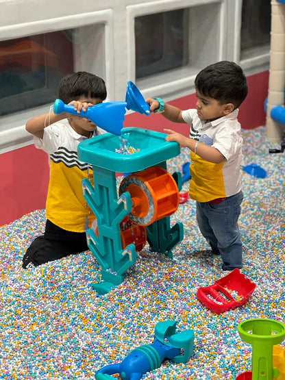 Two young children play with a water toy in a ball pit filled with colorful balls.