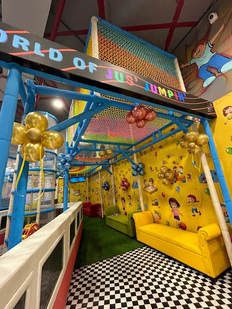 A colorful indoor playground with a soft play area, seating, and cartoon murals for children.