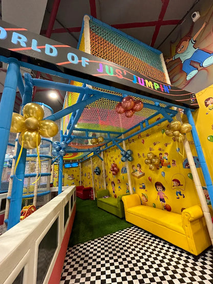 A colorful indoor playground with a soft play area, seating, and cartoon murals for children.
