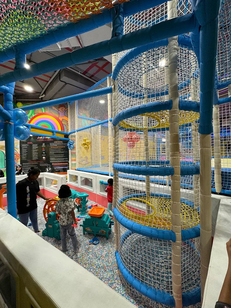 Children play in a colorful indoor playground with nets and slides.