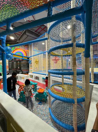 Children play in a colorful indoor playground with nets and slides.
