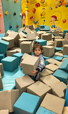 A young child sits in a ball pit filled with large foam blocks.