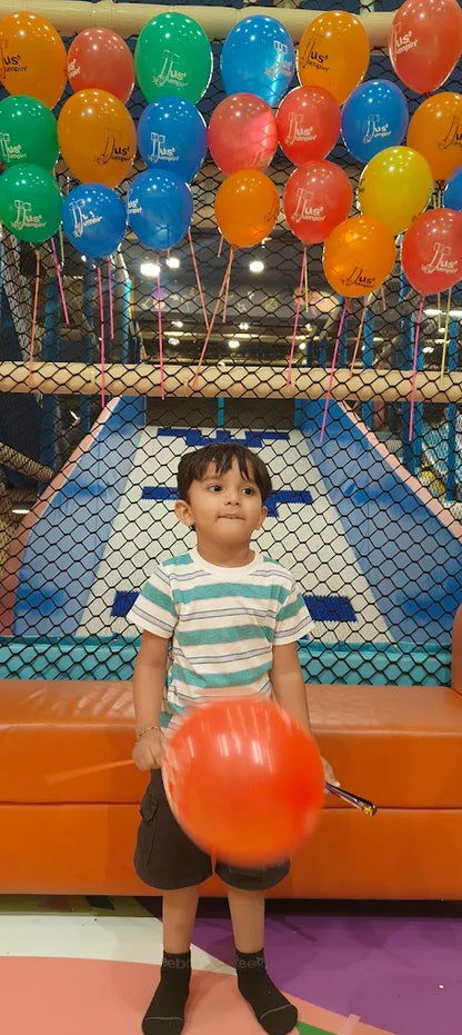 A young boy holds a large orange balloon in a colorful indoor play area.
