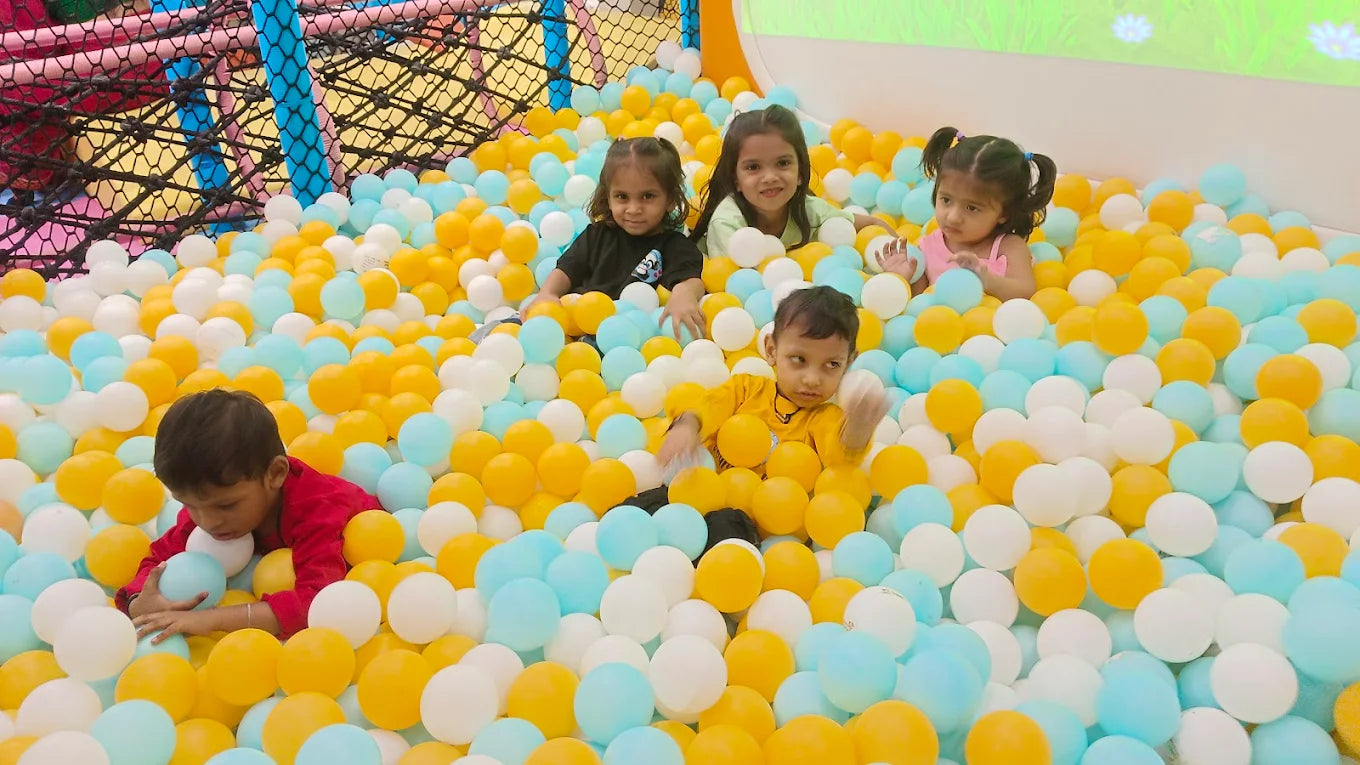 Children play in a ball pit filled with yellow, blue, and white balls.