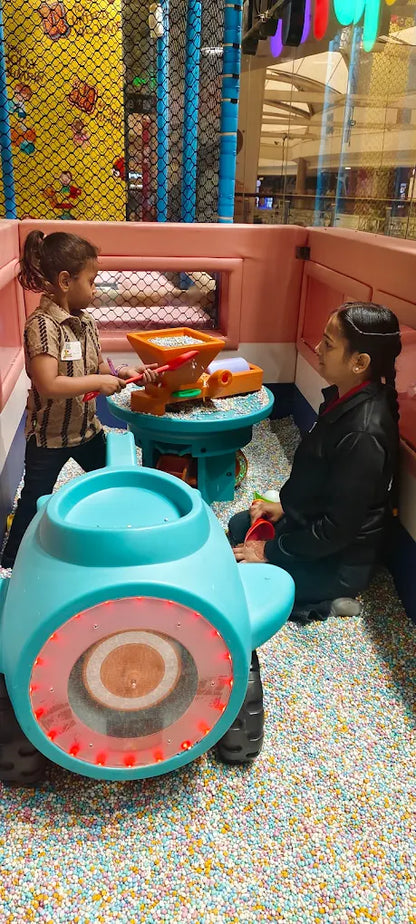Two young children play in a ball pit with a toy.