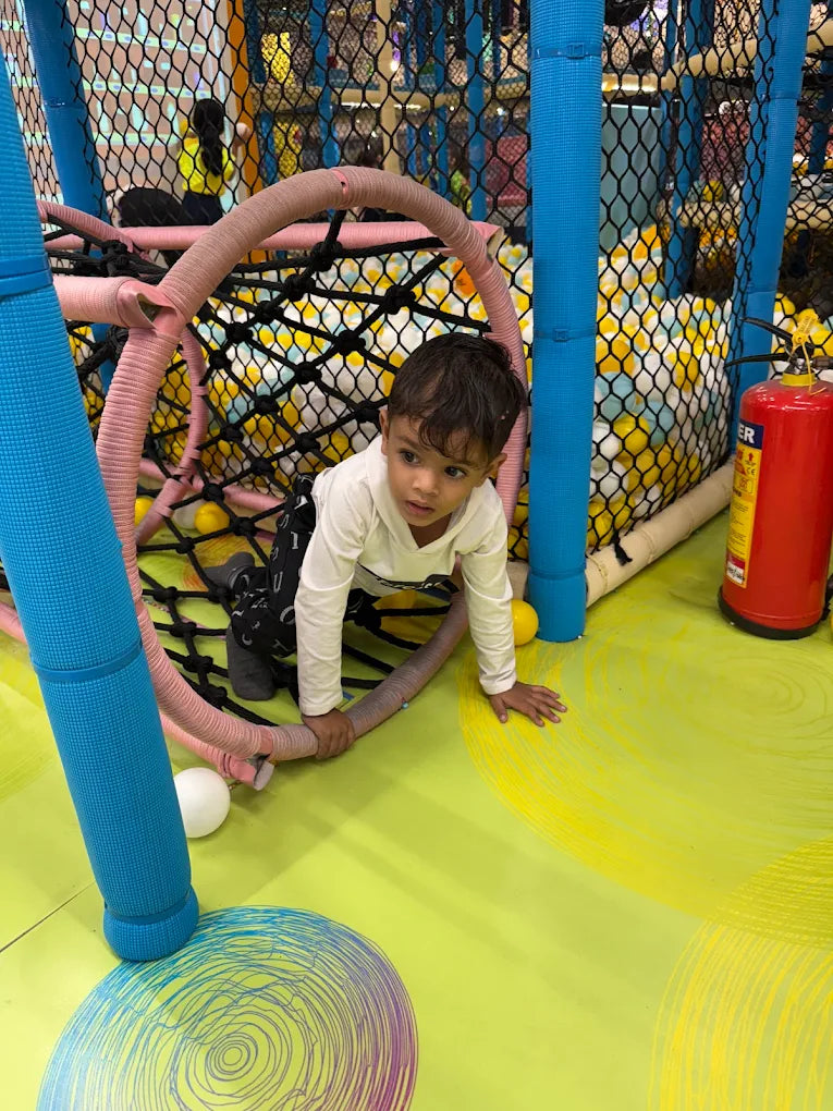 A young child crawls through a colorful indoor playground with a ball pit.