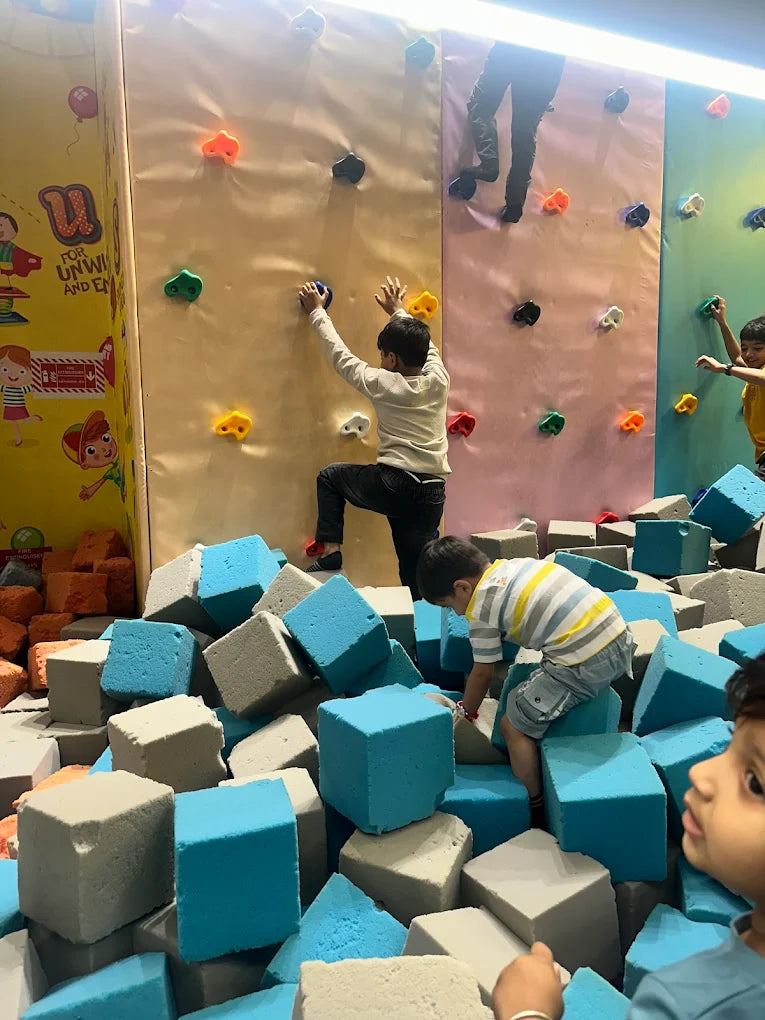 Children climb a colorful indoor rock wall and play in a foam pit.