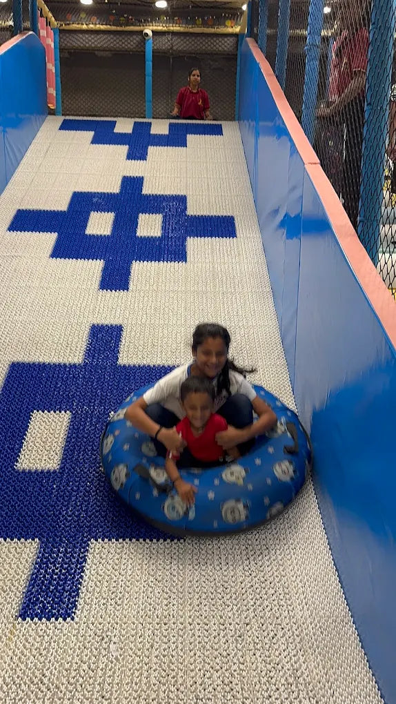Two children slide down a padded slope on a tube.