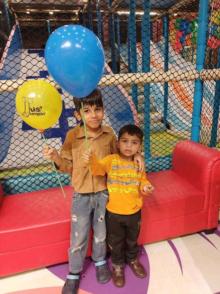 Two young boys hold balloons in a colorful indoor playground.