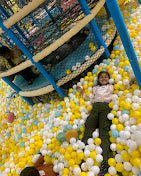 A child lies in a ball pit, smiling.