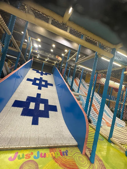 A colorful indoor playground slide with blue and white patterns, featuring the text "Jus' Jumpin'".