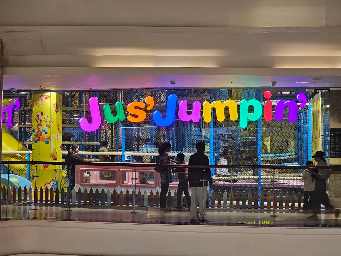 A colorful indoor playground with children playing, seen through a glass barrier.