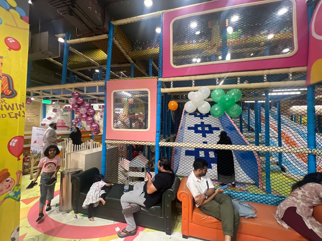 Children and adults enjoy a colorful indoor playground with slides and climbing structures.