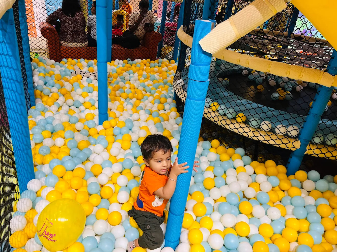 A toddler plays in a ball pit filled with yellow, blue, and white balls.
