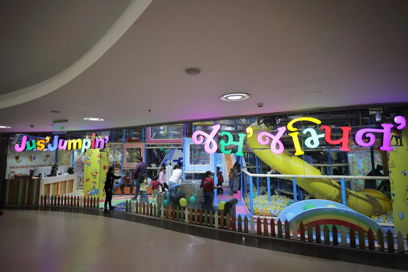 A colorful indoor play area for children with a "Jus' Jumpin'" sign and a slide into a ball pit.