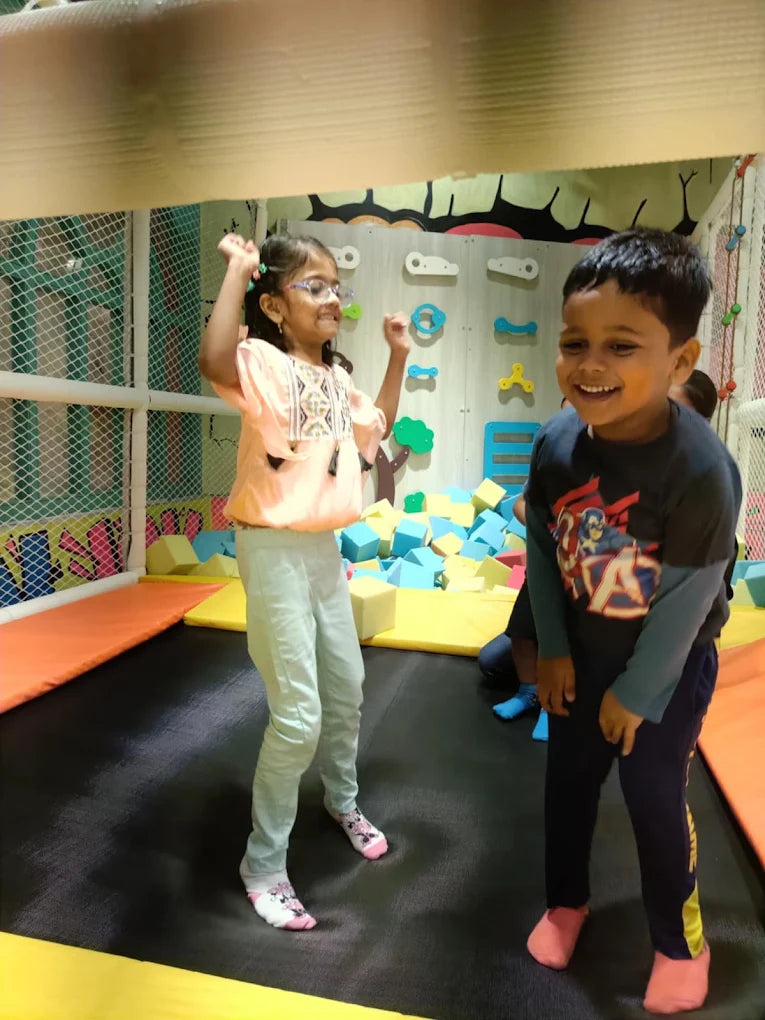 Two young children joyfully jump on a trampoline in an indoor play area.