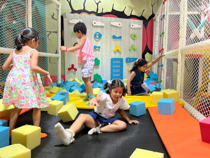 Young children play in a colorful indoor playground with foam blocks and climbing walls.