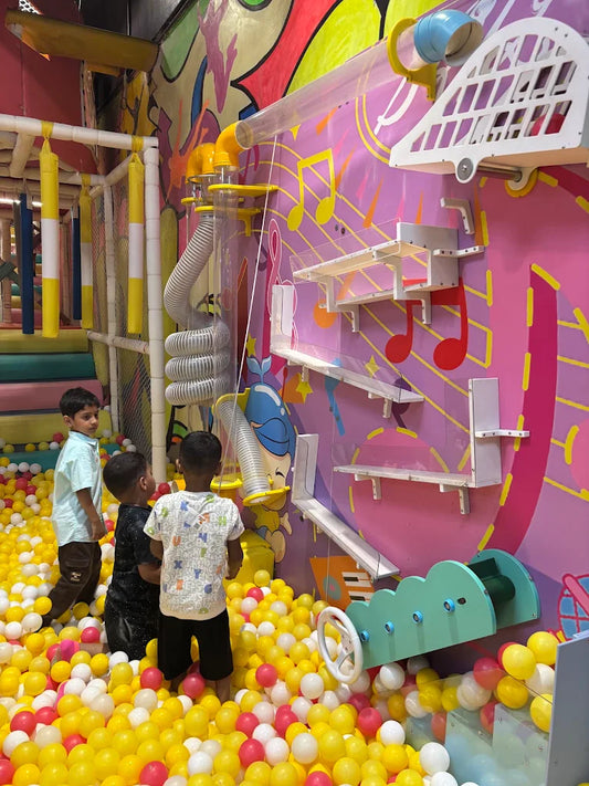 Children play in a colorful ball pit with a musical-themed wall and tube system.