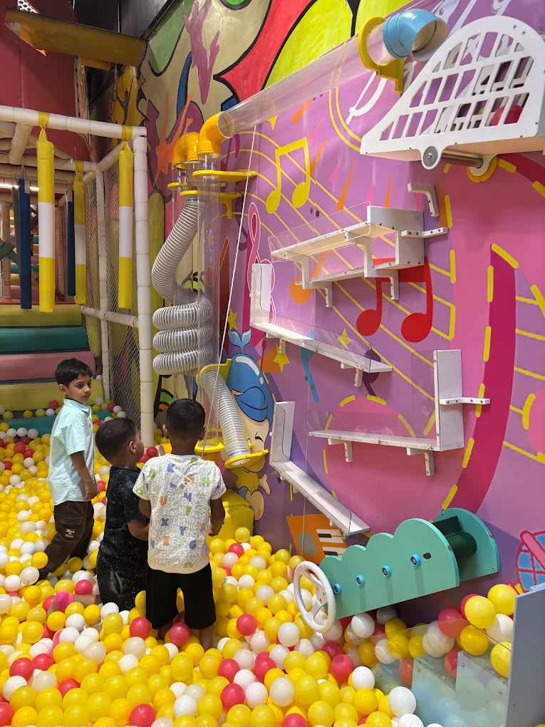 Children play in a colorful ball pit with a musical-themed wall and tube system.