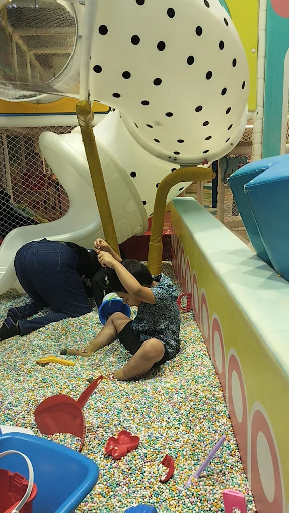 Children play in a ball pit with slides and toys.