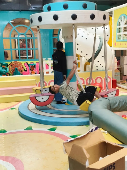 A young boy swings on a playground ride while another child stands nearby.