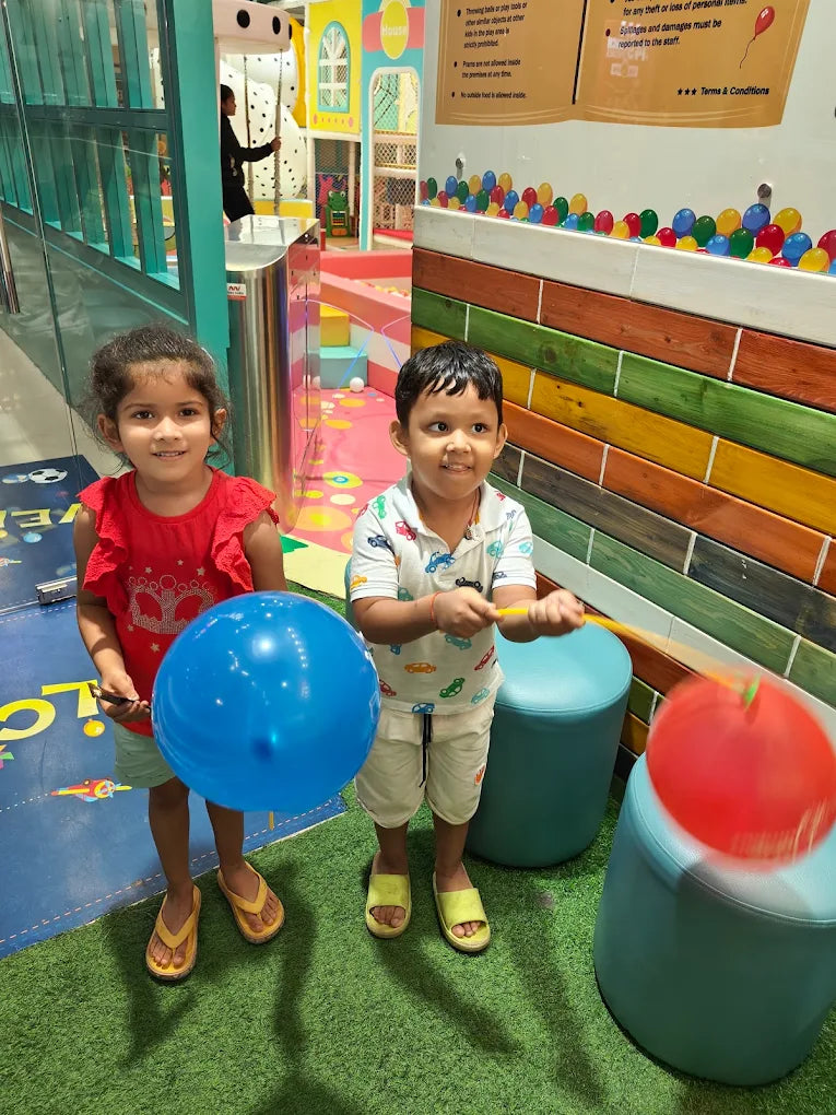 Two young children play with balloons in a colorful indoor play area.