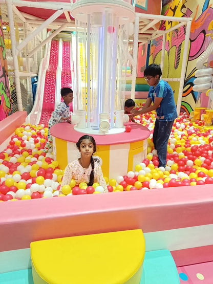 Children play in a colorful ball pit with slides and a ball dispenser.
