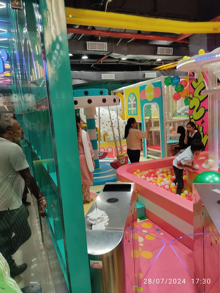 Children play in a colorful ball pit at an indoor playground. Adults supervise in the background.