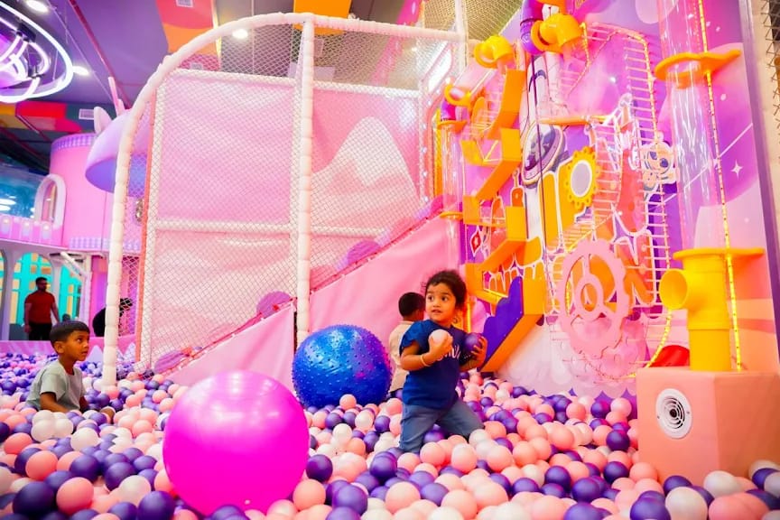 Children play in a colorful ball pit at an indoor playground.