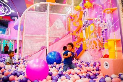Children play in a colorful ball pit at an indoor playground.