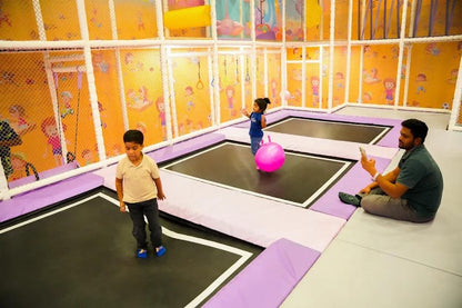 Children and an adult are in a brightly colored indoor trampoline park.