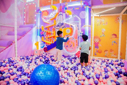 Two young boys play in a colorful ball pit in an indoor playground.
