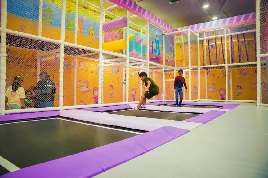 Children jump on trampolines in a colorful indoor play area.