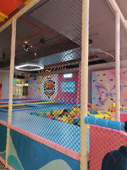 Children play in a colorful indoor trampoline park with foam pits and a climbing wall.