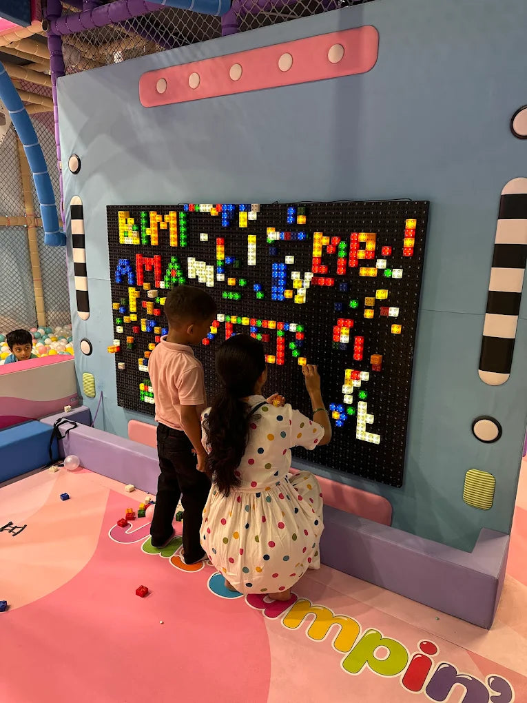 Children play with a light-up brick wall in a colorful indoor playground.