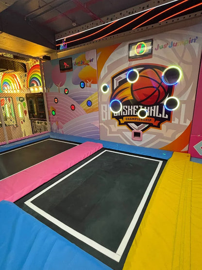 An indoor trampoline park with a basketball game and colorful decorations.