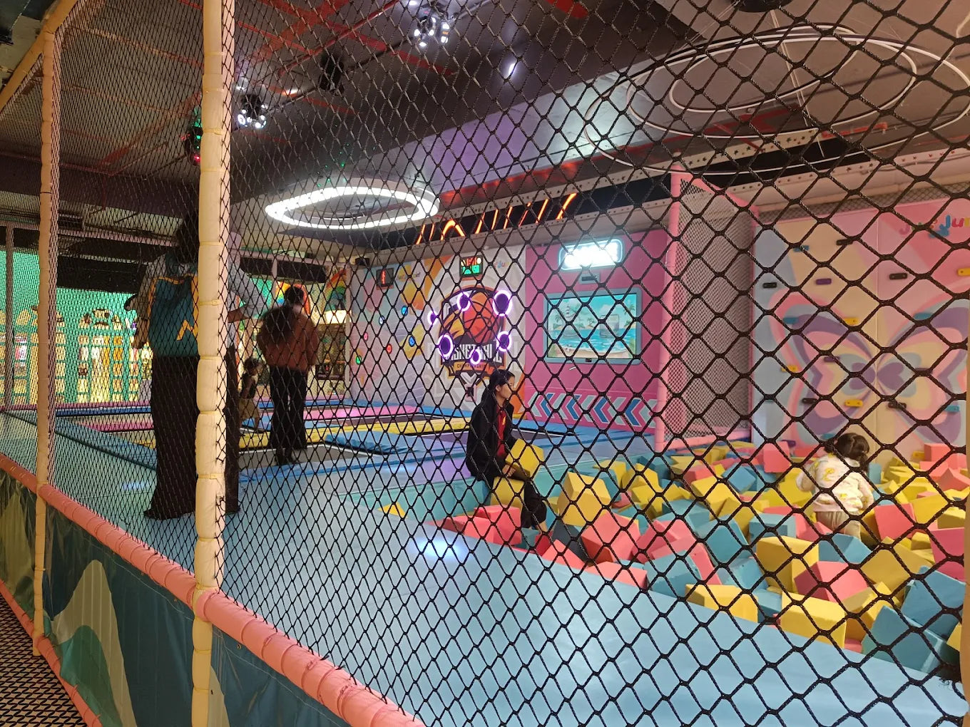 Children play in a colorful indoor trampoline park with a foam pit.