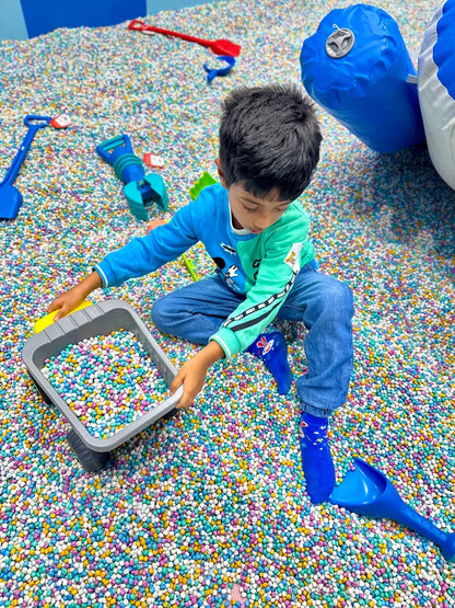A young boy plays in a ball pit filled with colorful balls, holding a toy truck.