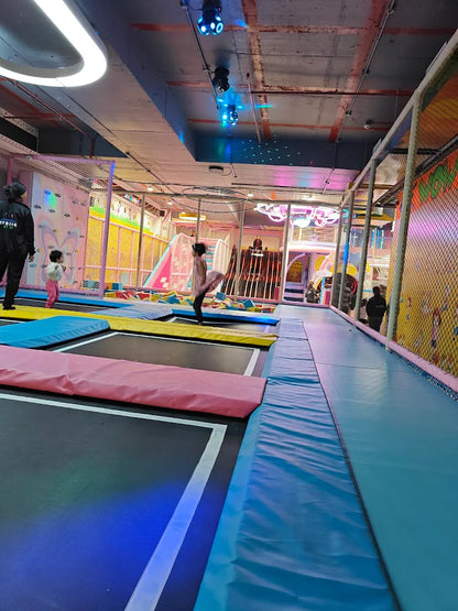 Children jump on trampolines in a colorful indoor play area with slides and climbing structures.