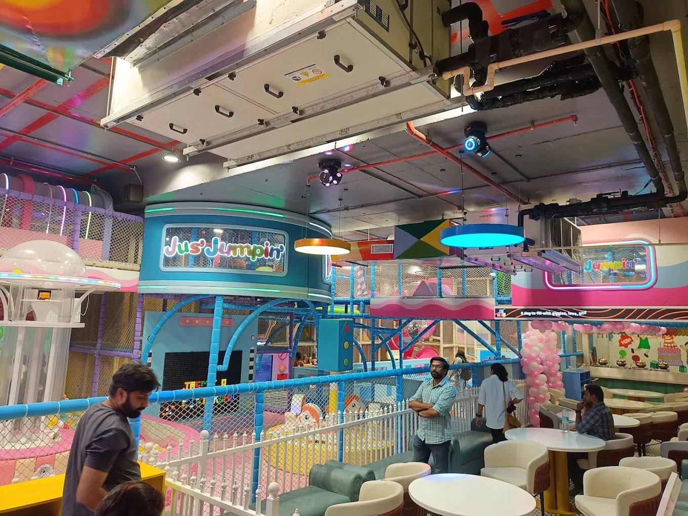 A vibrant indoor playground with colorful structures and a few adults enjoying the space.