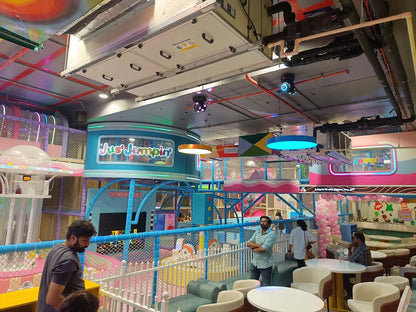 A vibrant indoor playground with colorful structures and a few adults enjoying the space.