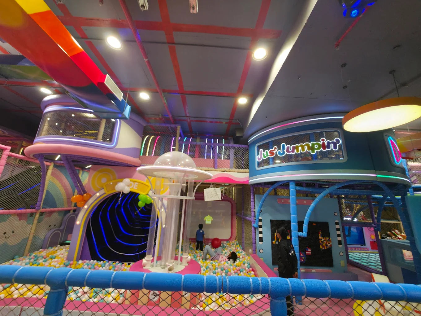 Children play in a colorful indoor playground with ball pits and climbing structures.